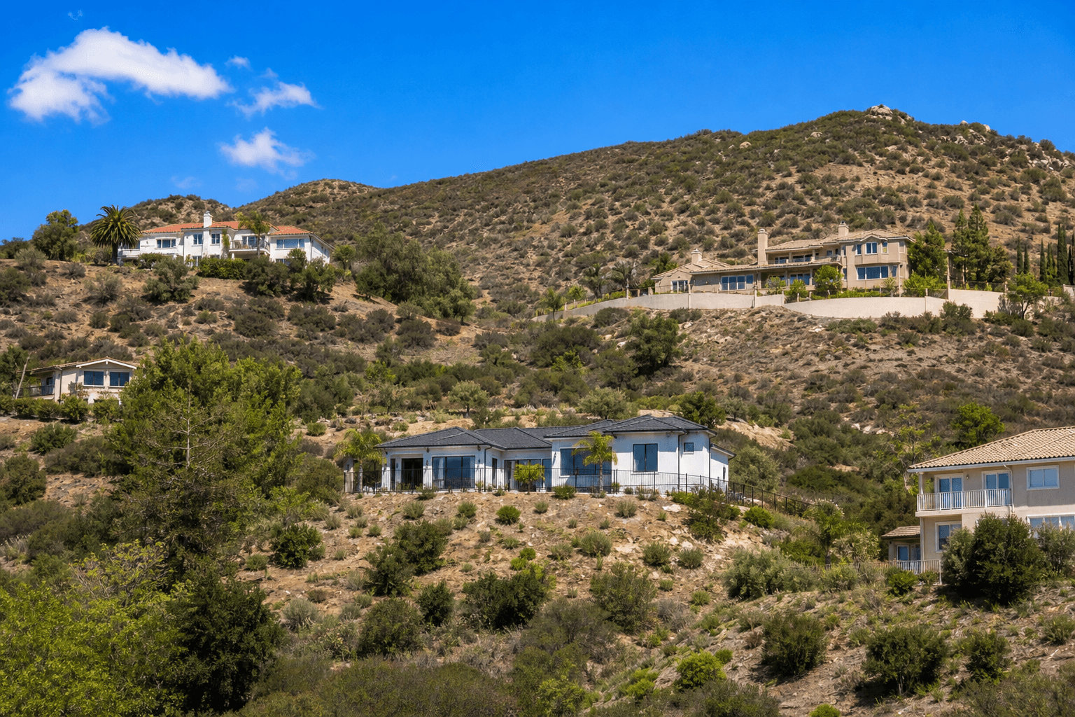 Murrieta hillside homes bordered by cleared defensible space against dry chaparral foothills under a clear sky.