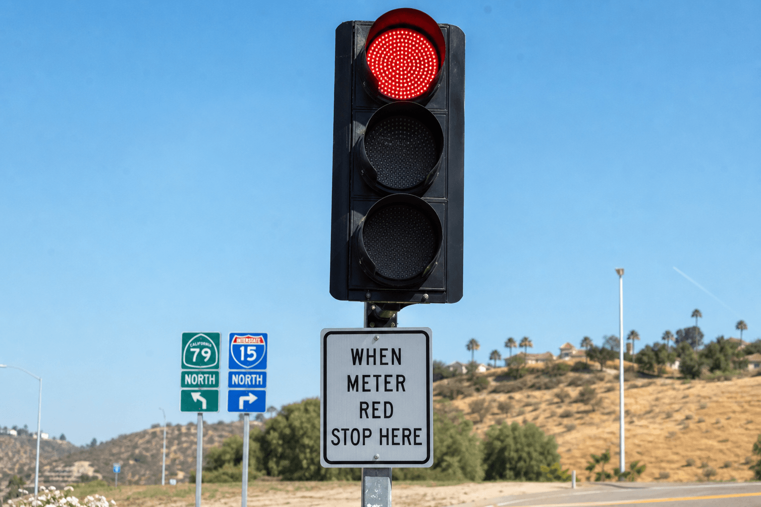 Close-up of a ramp meter traffic signal with red and green lights at a Temecula I-15 on-ramp.